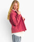 A woman wearing a pink quilted corduroy jacket, styled with a white top and light blue jeans, posing against a plain white studio background.