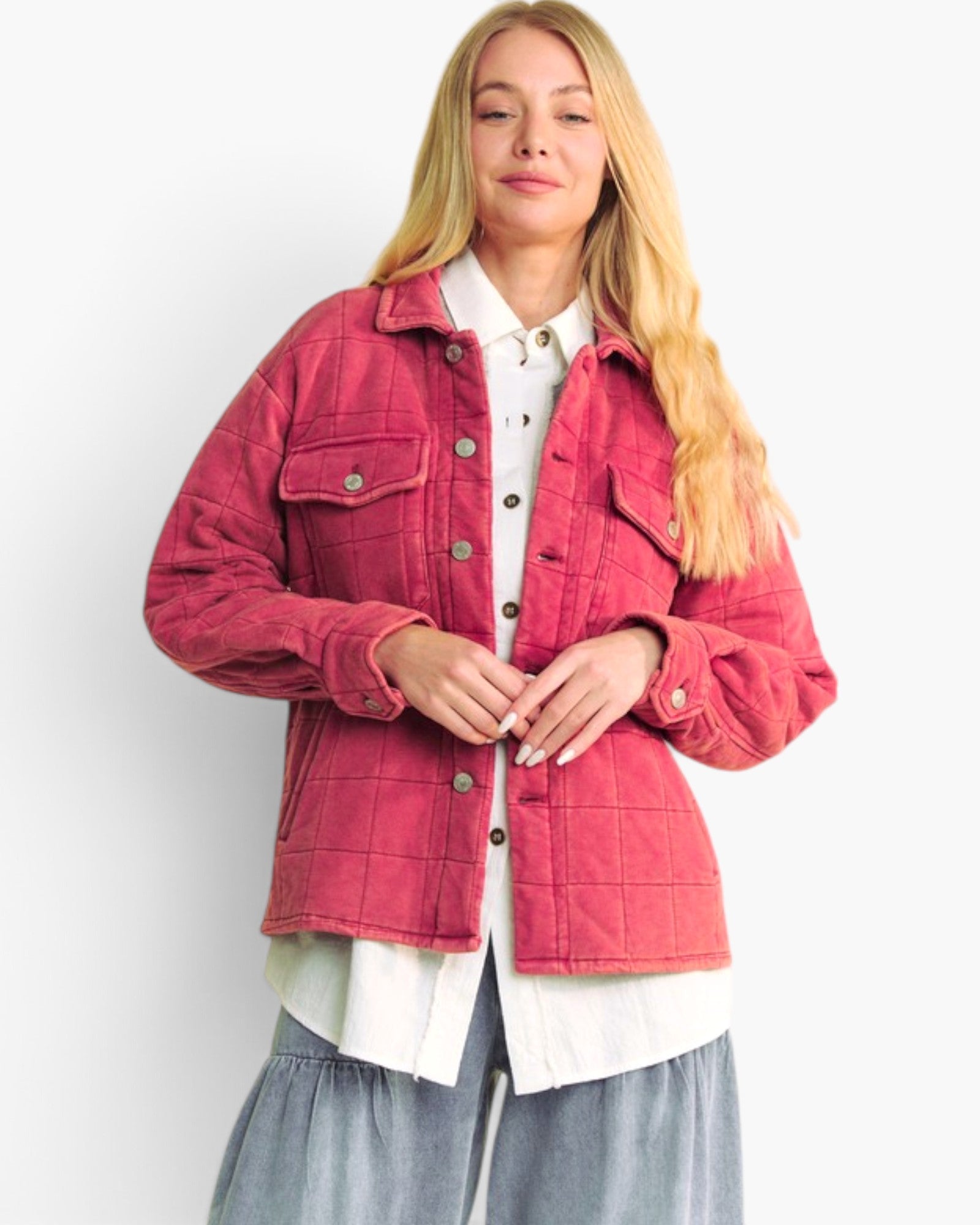 A woman wearing a quilted pink jacket over a white collared shirt and gray pants, standing against a plain white studio background.