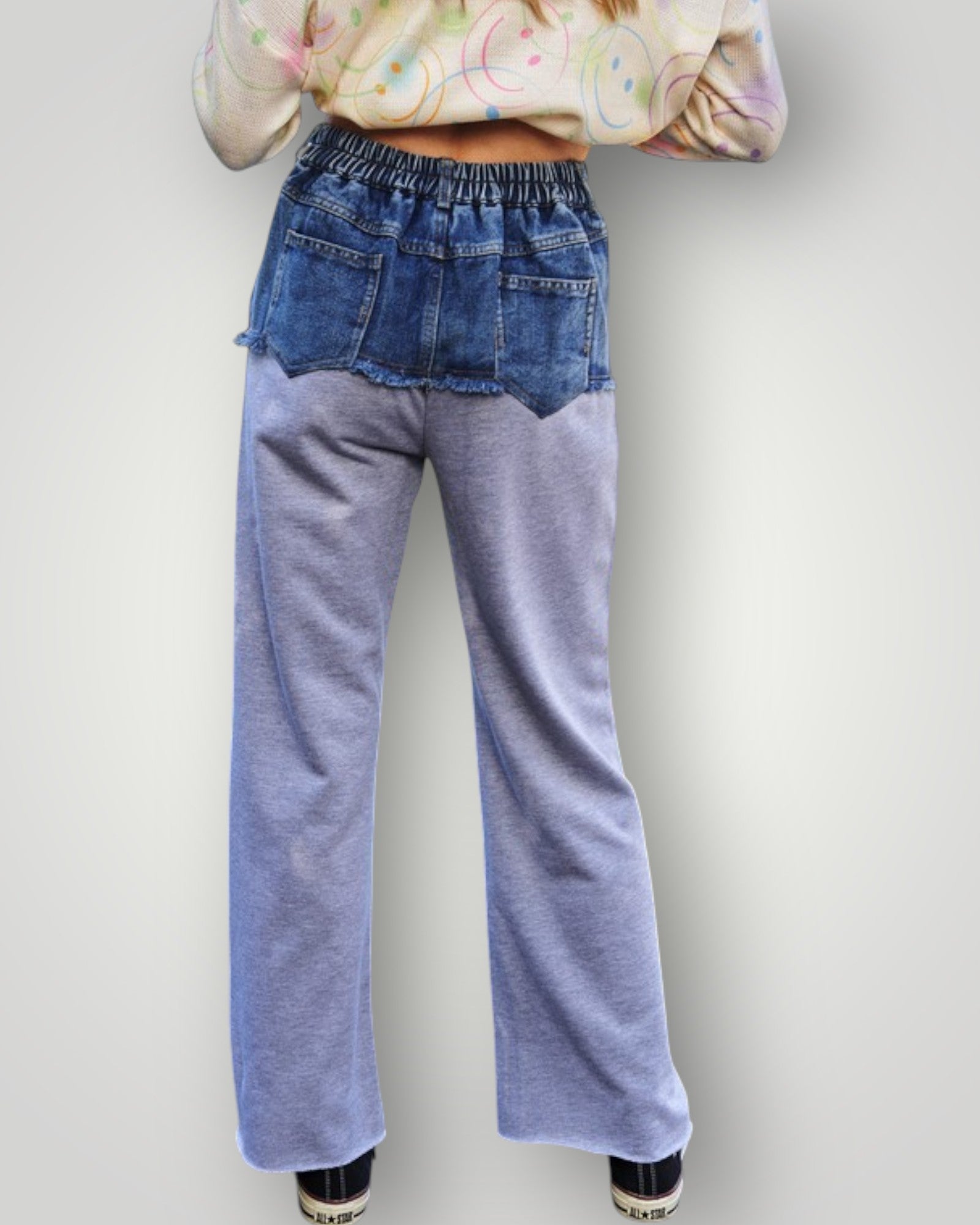Person wearing blue jeans and a colorful top on a plain background