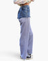 A person shown from the waist down wearing wide-leg pants with a color-blocked design: medium blue denim on the upper portion and a heathered periwinkle blue lower portion, paired with black sneakers against a plain white studio background.