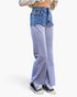 A person shown from the waist down wearing layered pants with a blue denim top half and light blue heathered wide-leg bottom half, paired with black sneakers against a plain white background.