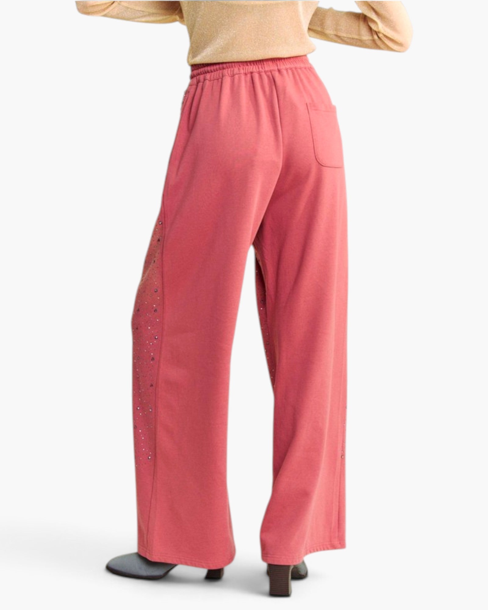 A person shown from the back wearing loose, wide-leg pink pants with a small side embellishment and a tan top, photographed against a plain light background.