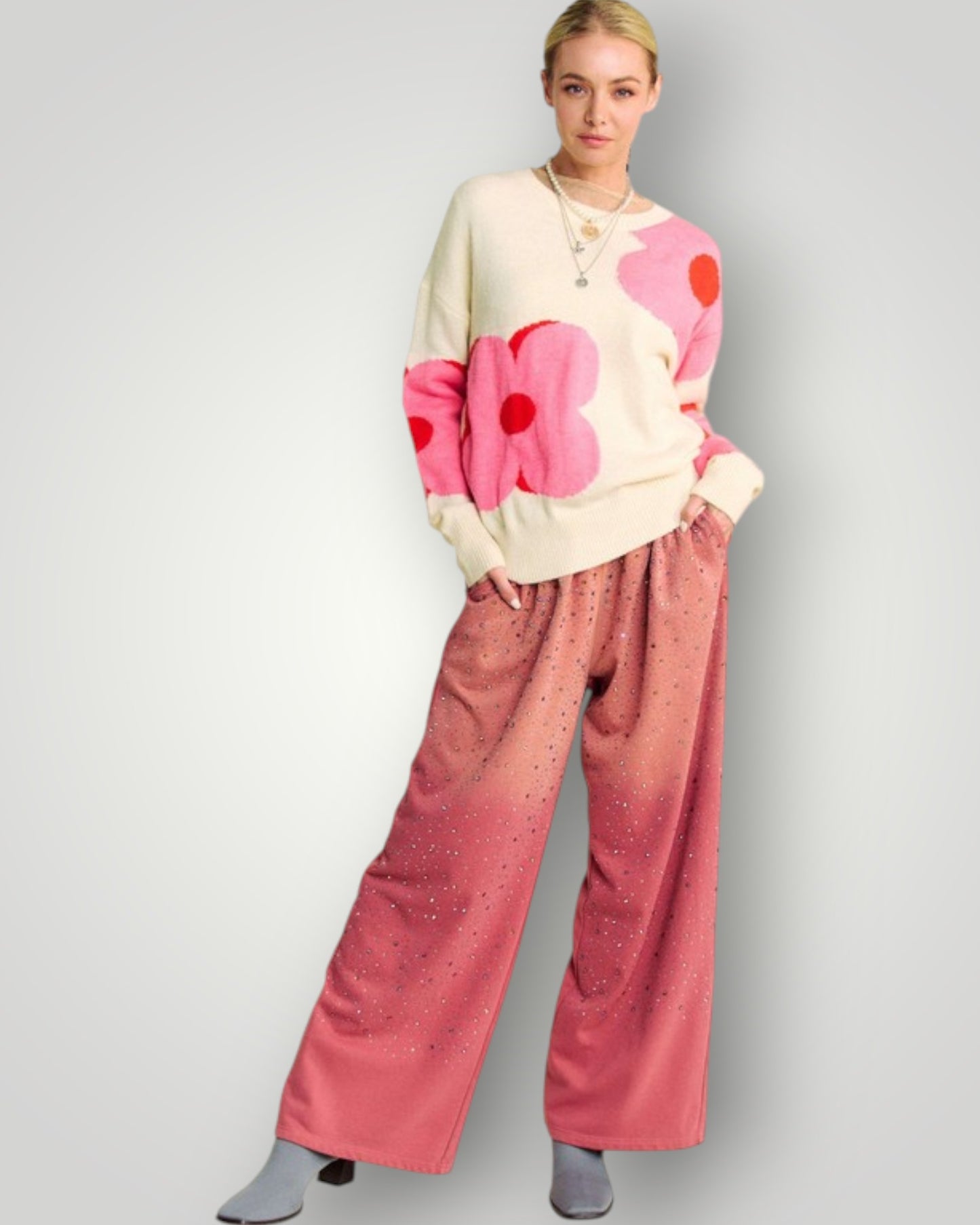 Person wearing a cream sweater with pink heart patterns and pink pants on a light gray background