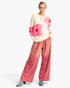A model wearing a cream knit sweater with large pink and red flower motifs, paired with wide-leg pink gradient pants featuring small silver rhinestone embellishments, and gray pointed-toe boots, against a plain white background.