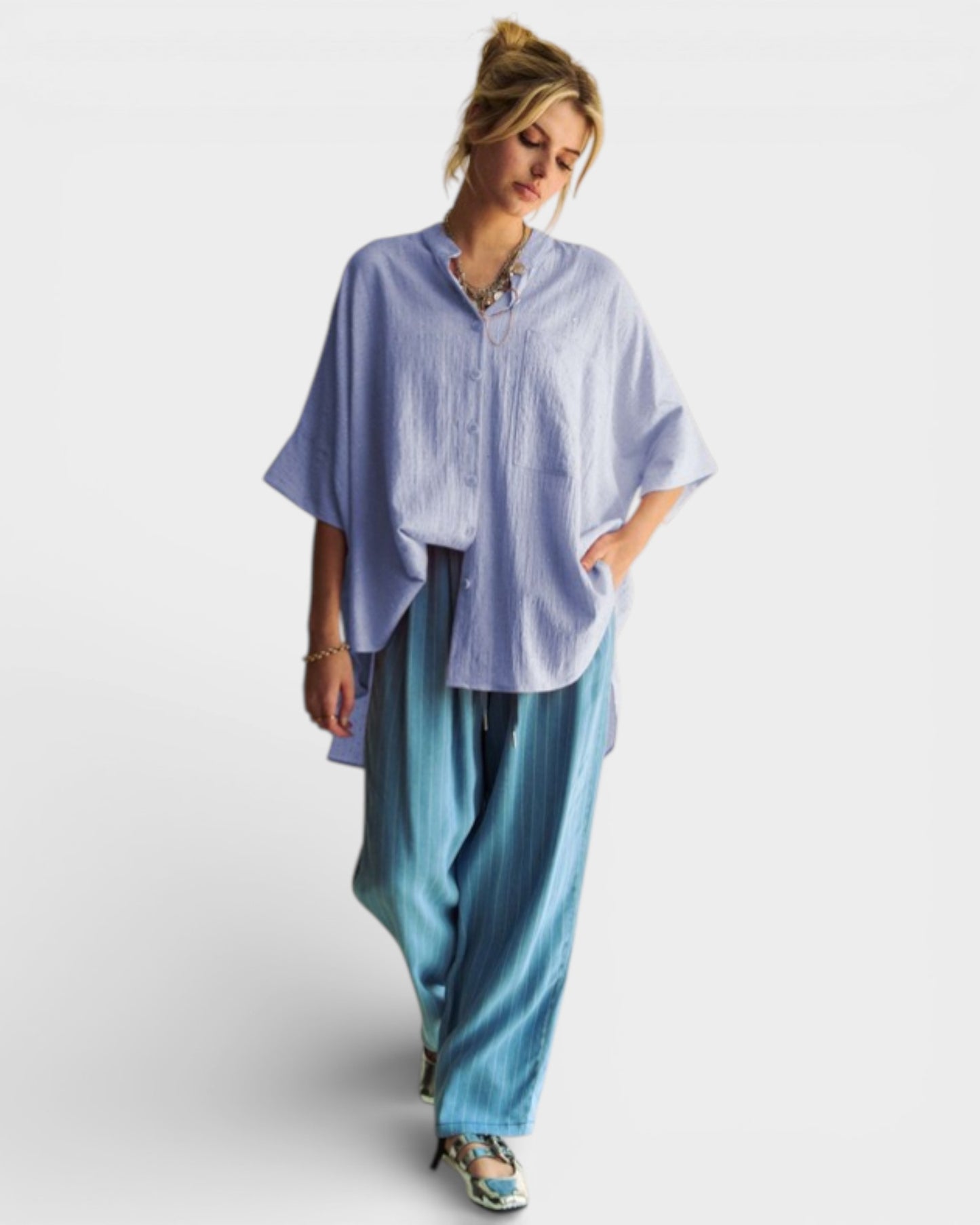 Woman wearing a light blue oversized shirt and blue pants on a white background