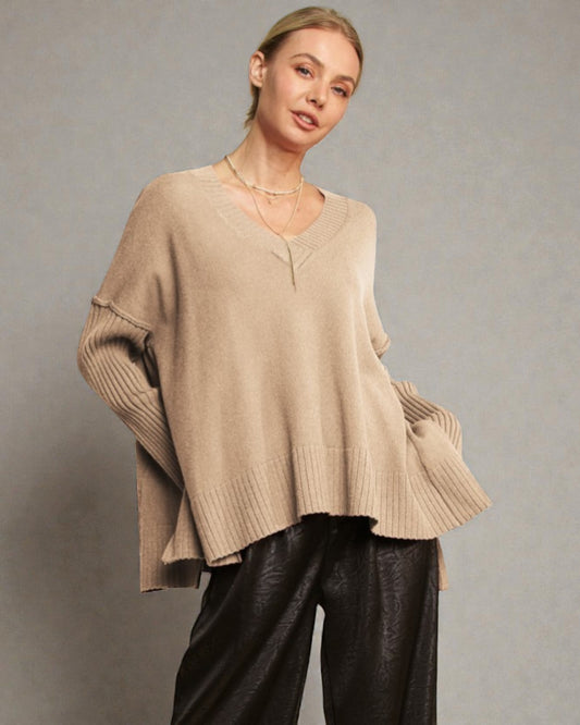 Woman wearing a beige sweater and black pants against a gray background