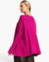 A woman wearing a bright magenta pink knit sweater, shown from a side-back angle against a clean white background.