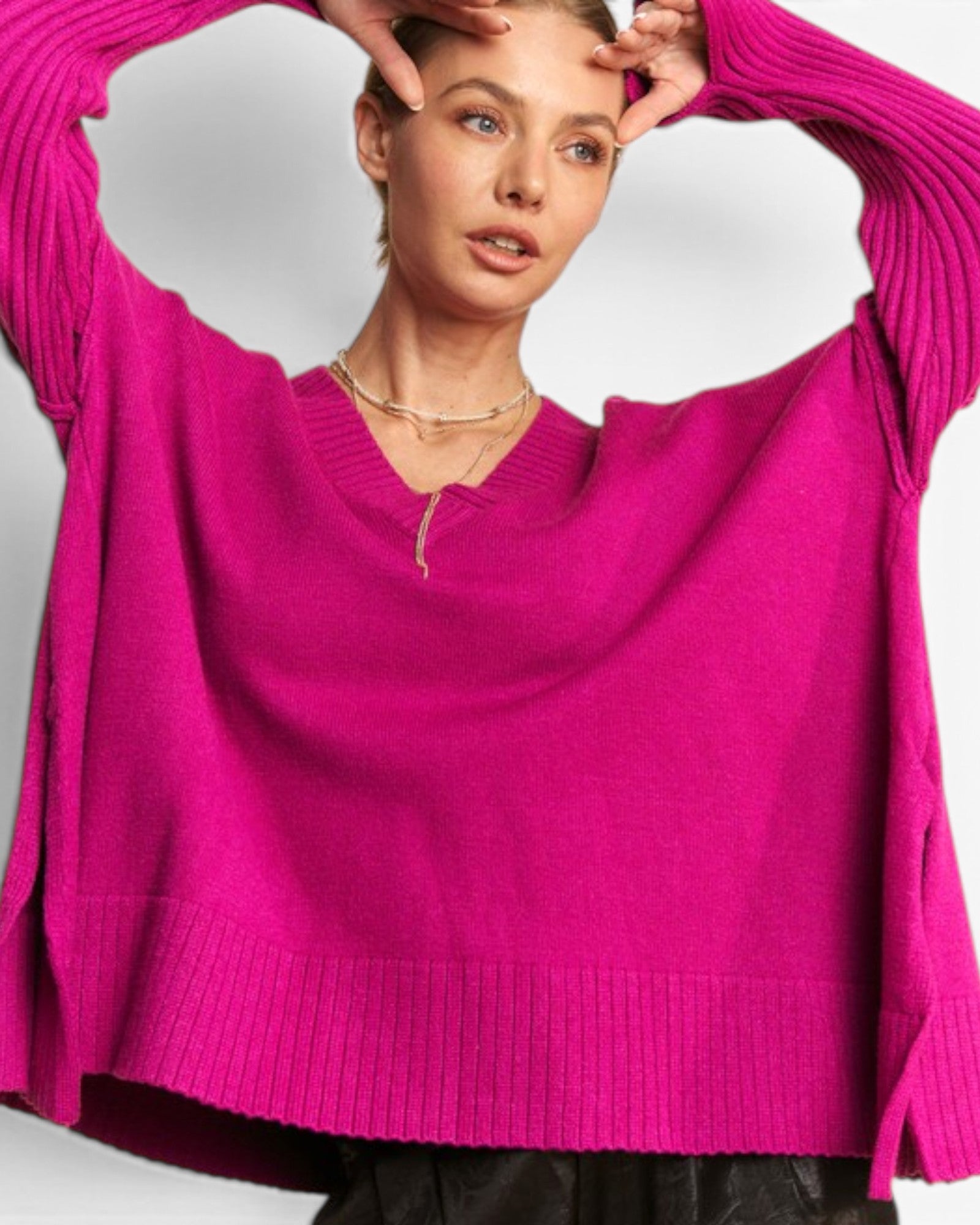 A woman wearing a bright fuchsia pink knit sweater with a V-neck and wide sleeves, posed against a light gray studio background.