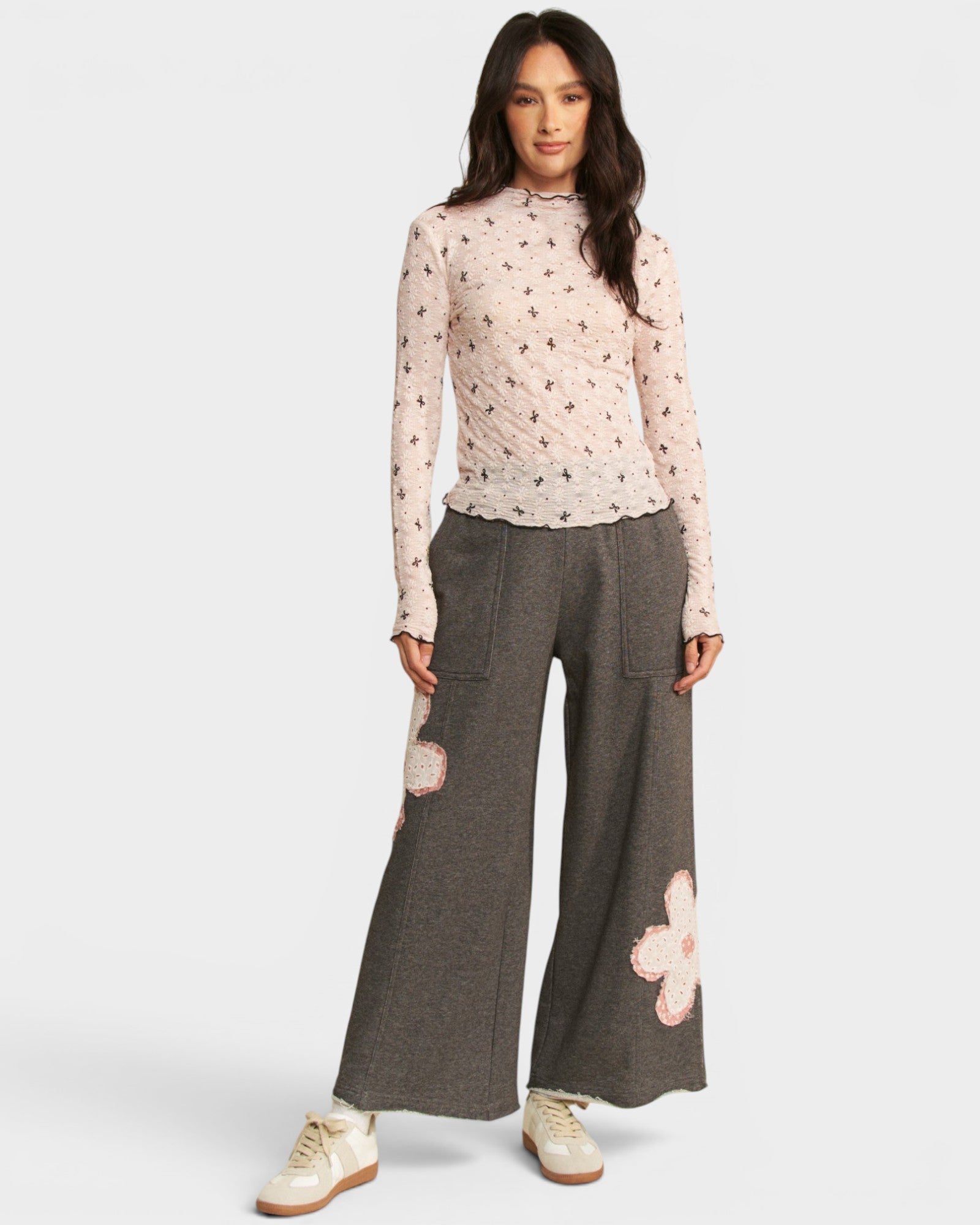 Woman wearing a floral top and wide-leg pants with flower details on a white background