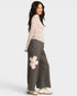 Woman wearing a light pink floral top and gray wide-leg pants with a flower design on a white background
