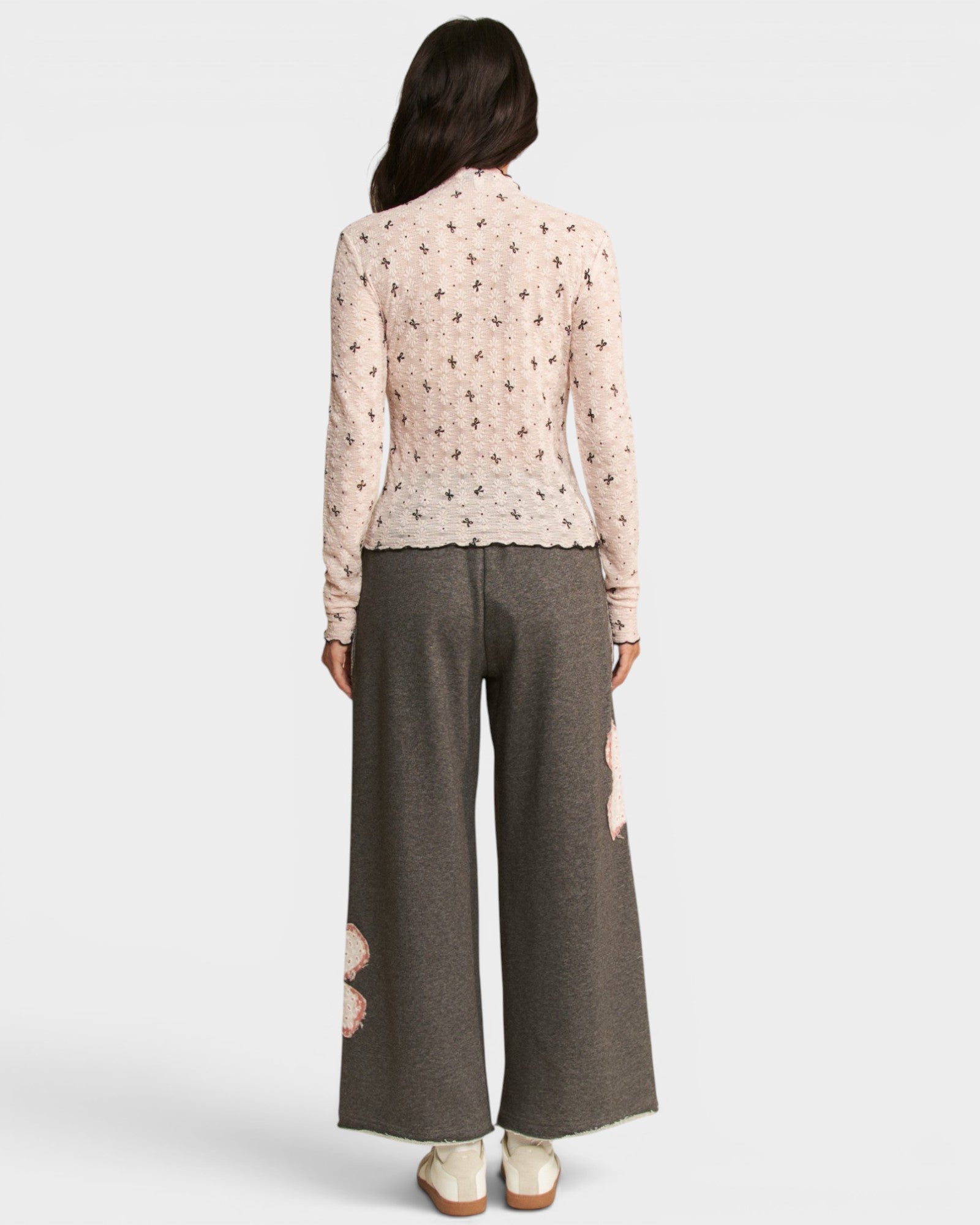 Person wearing a light pink floral blouse and gray wide-leg pants on a white background