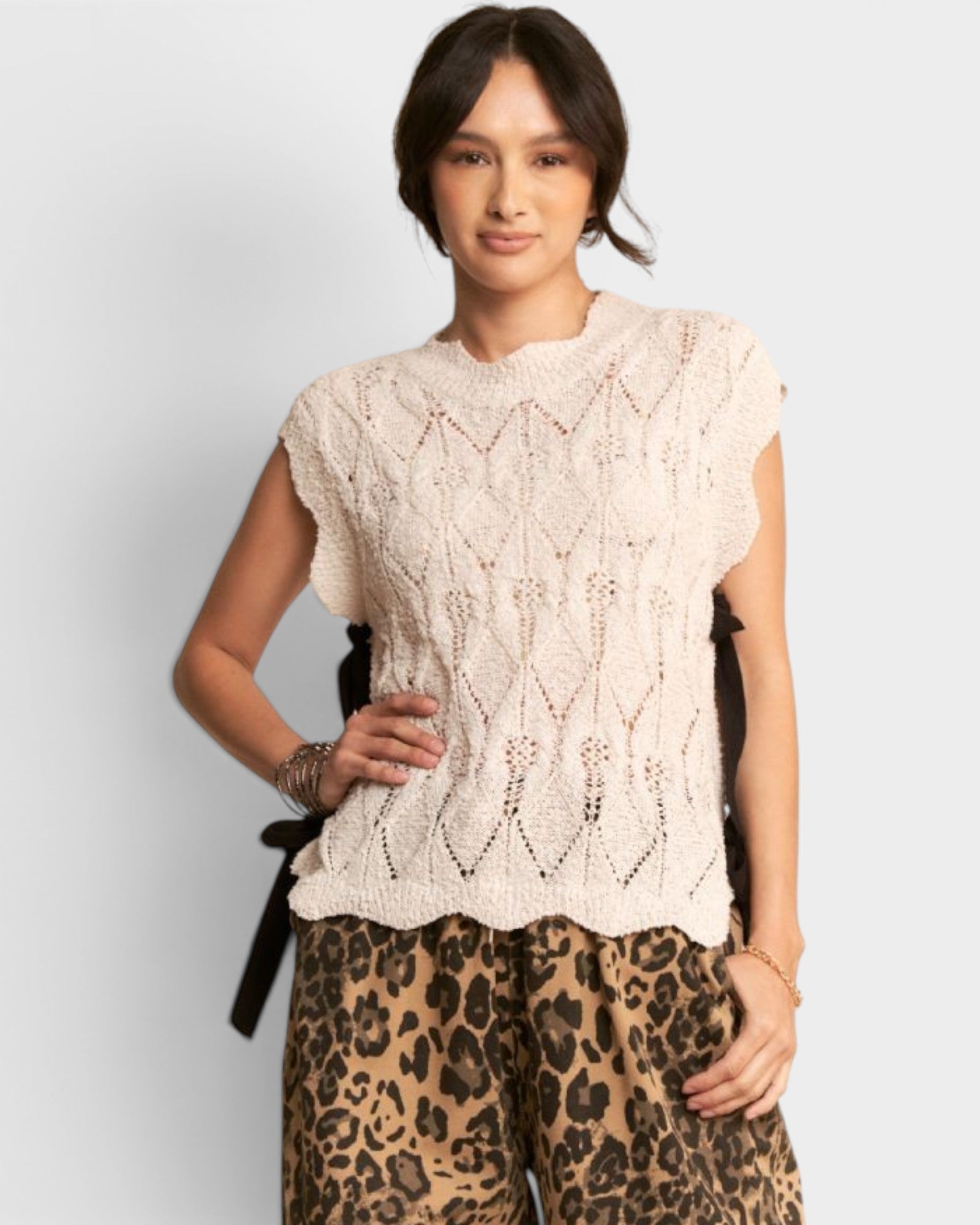 Woman wearing a beige lace top and leopard print pants on a plain background