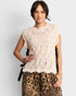 Woman wearing a beige lace top and leopard print pants on a plain background