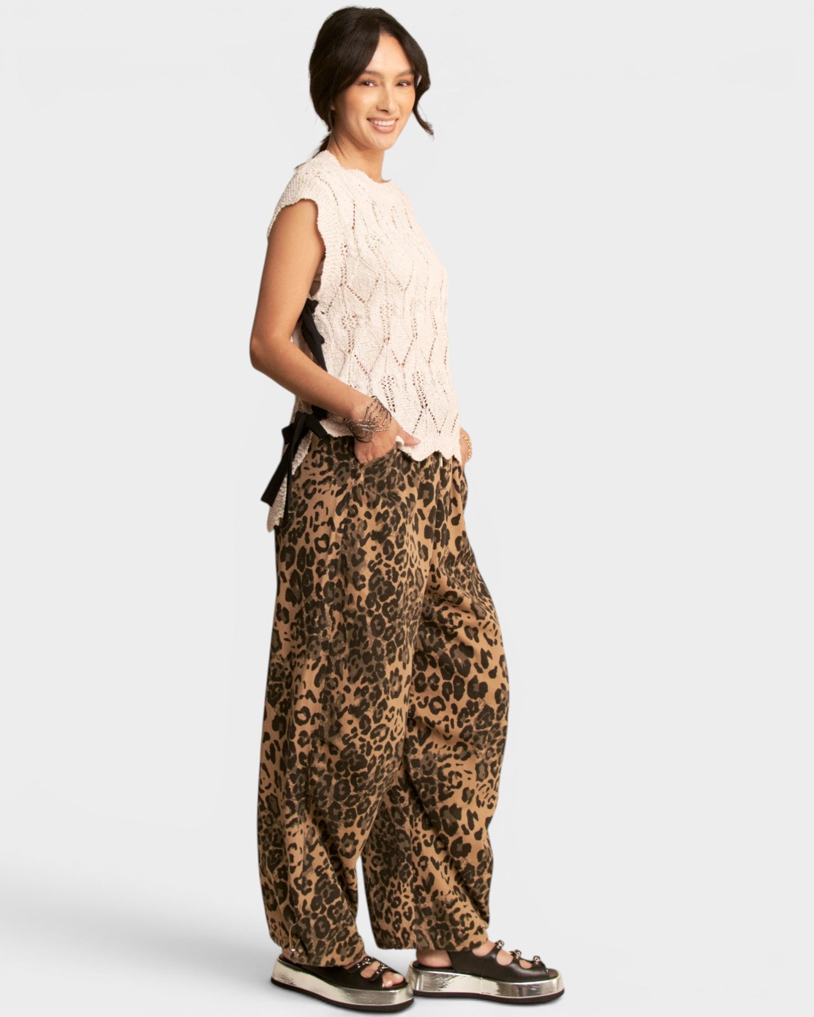Woman wearing a white sleeveless top and leopard print pants on a white background