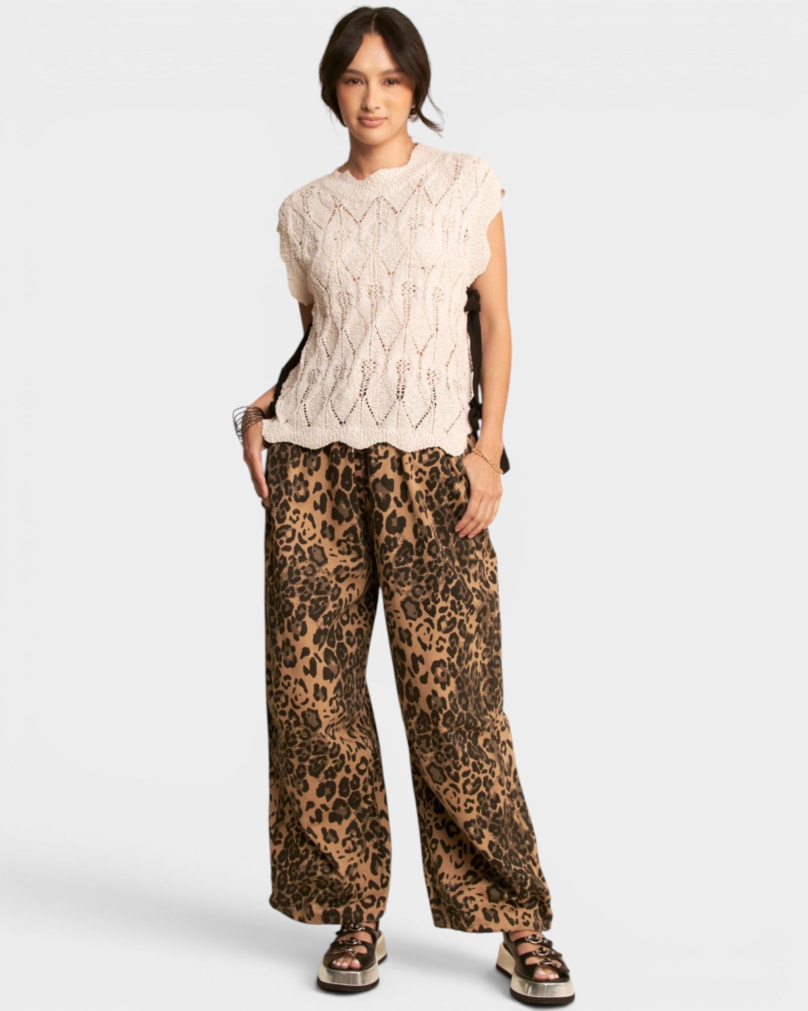 Woman wearing a cream sleeveless top and leopard print pants on a white background
