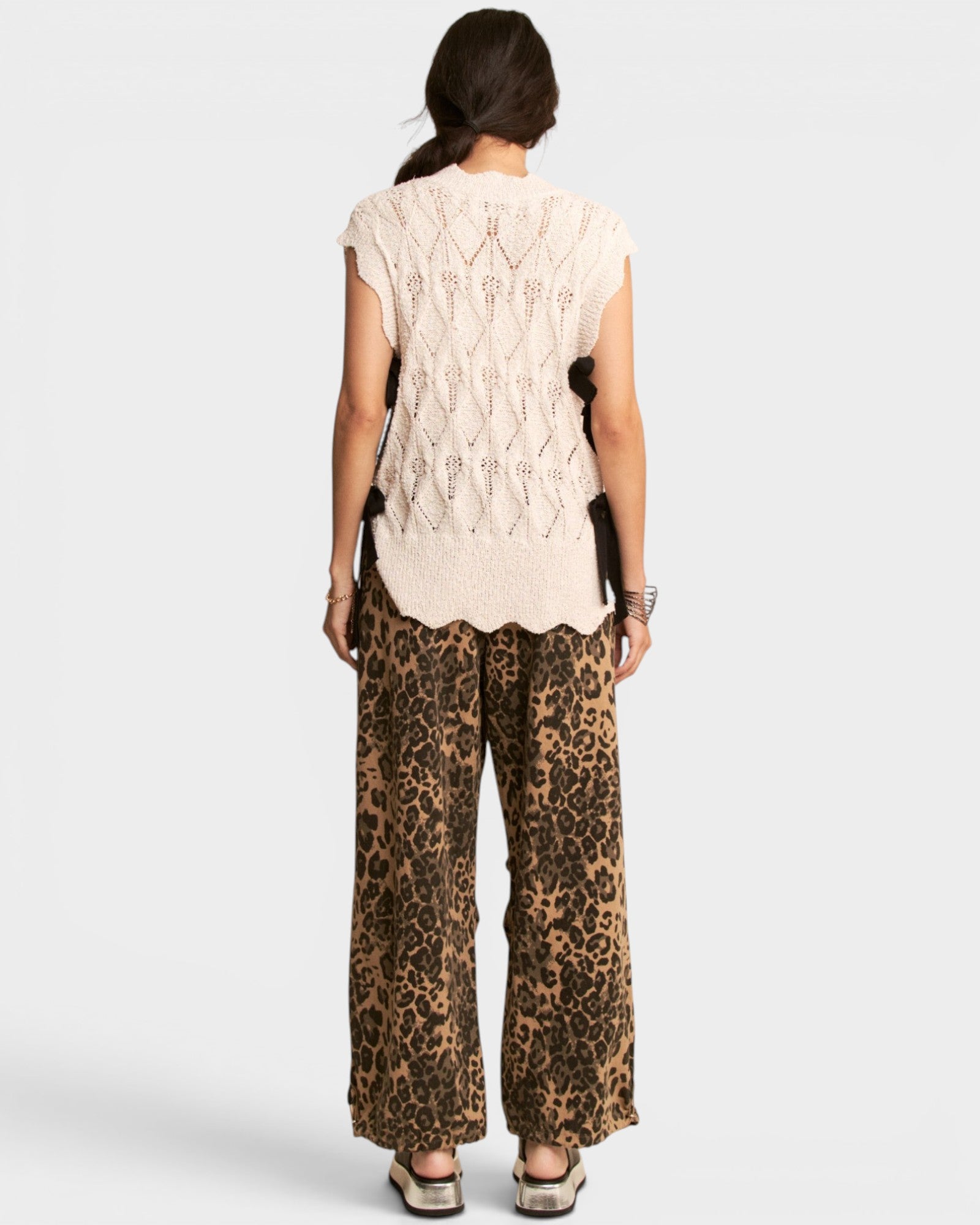 Person wearing a beige sleeveless top and leopard print pants on a white background