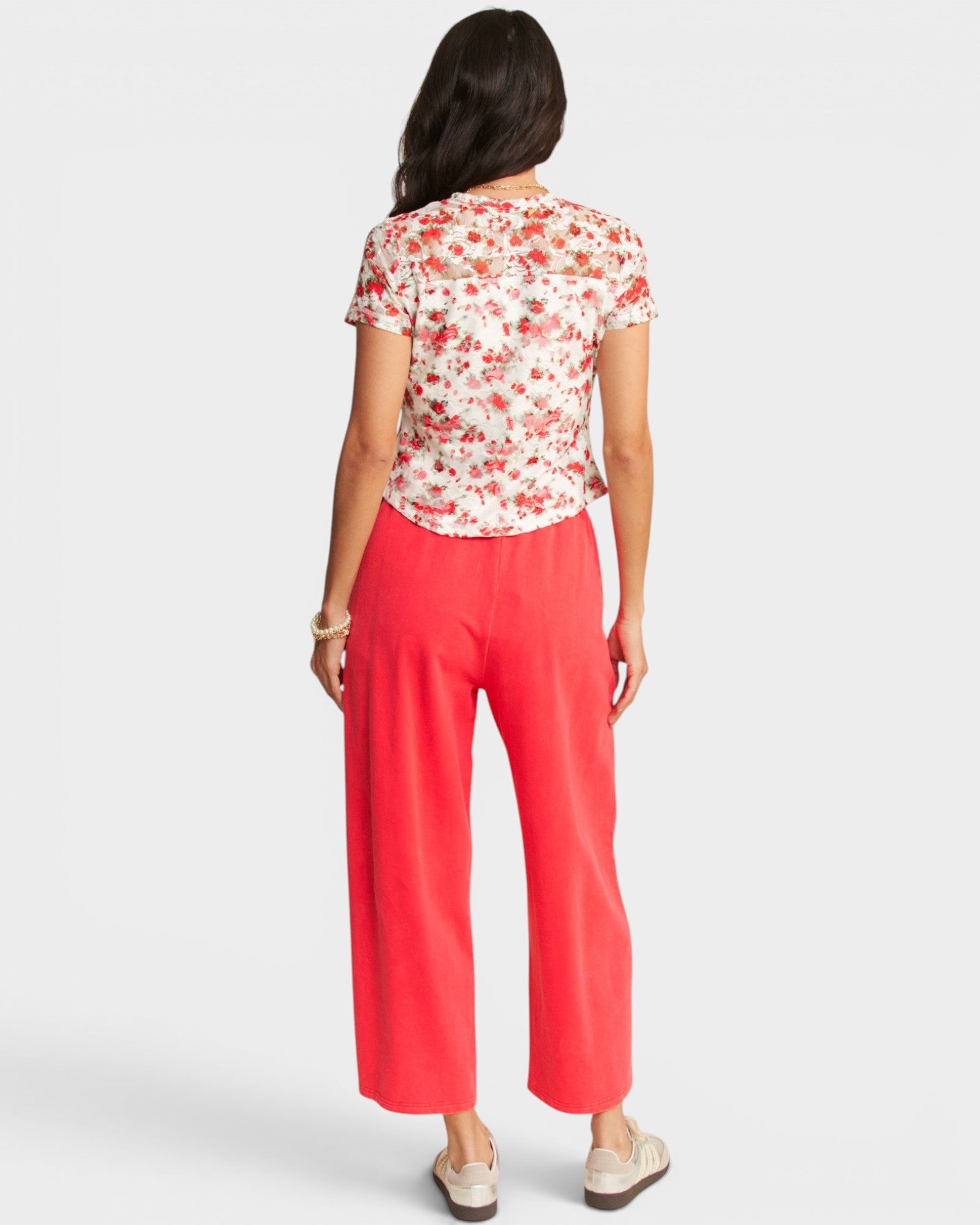 Woman wearing a floral top and coral pants on a white background