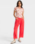 Woman wearing a floral top and coral pants on a white background