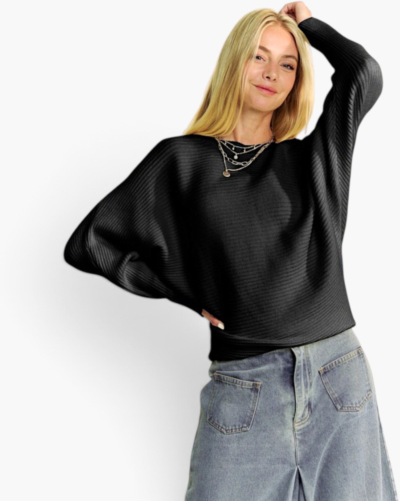 A woman wearing a black ribbed knit long-sleeve sweater with wide batwing sleeves and light-wash blue jeans, posed against a plain white studio background.