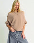 Woman wearing a beige sweater and blue jeans against a plain background