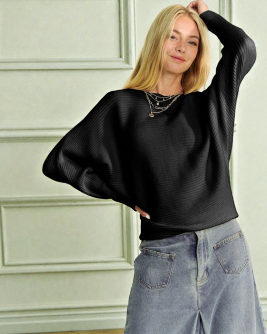 Woman wearing a black sweater and blue jeans against a light green wall.
