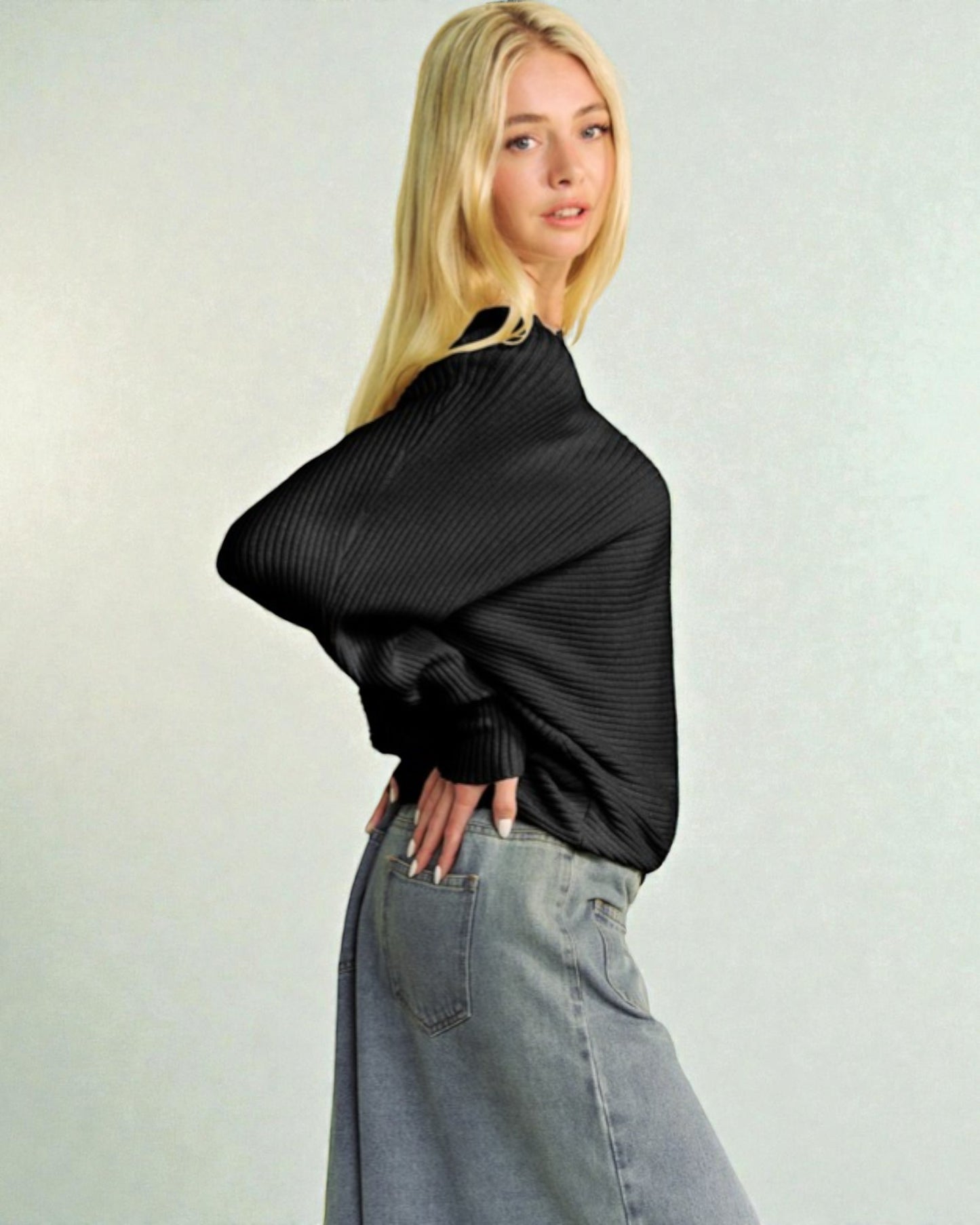 Woman wearing a black ribbed sweater and light blue jeans against a plain background