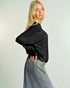 Woman wearing a black ribbed sweater and light blue jeans against a plain background