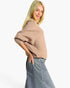 A blonde model wearing a beige ribbed knit sweater and a blue denim skirt, photographed against a clean white studio background.