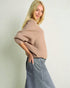 Woman wearing a beige sweater and blue jeans against a plain background