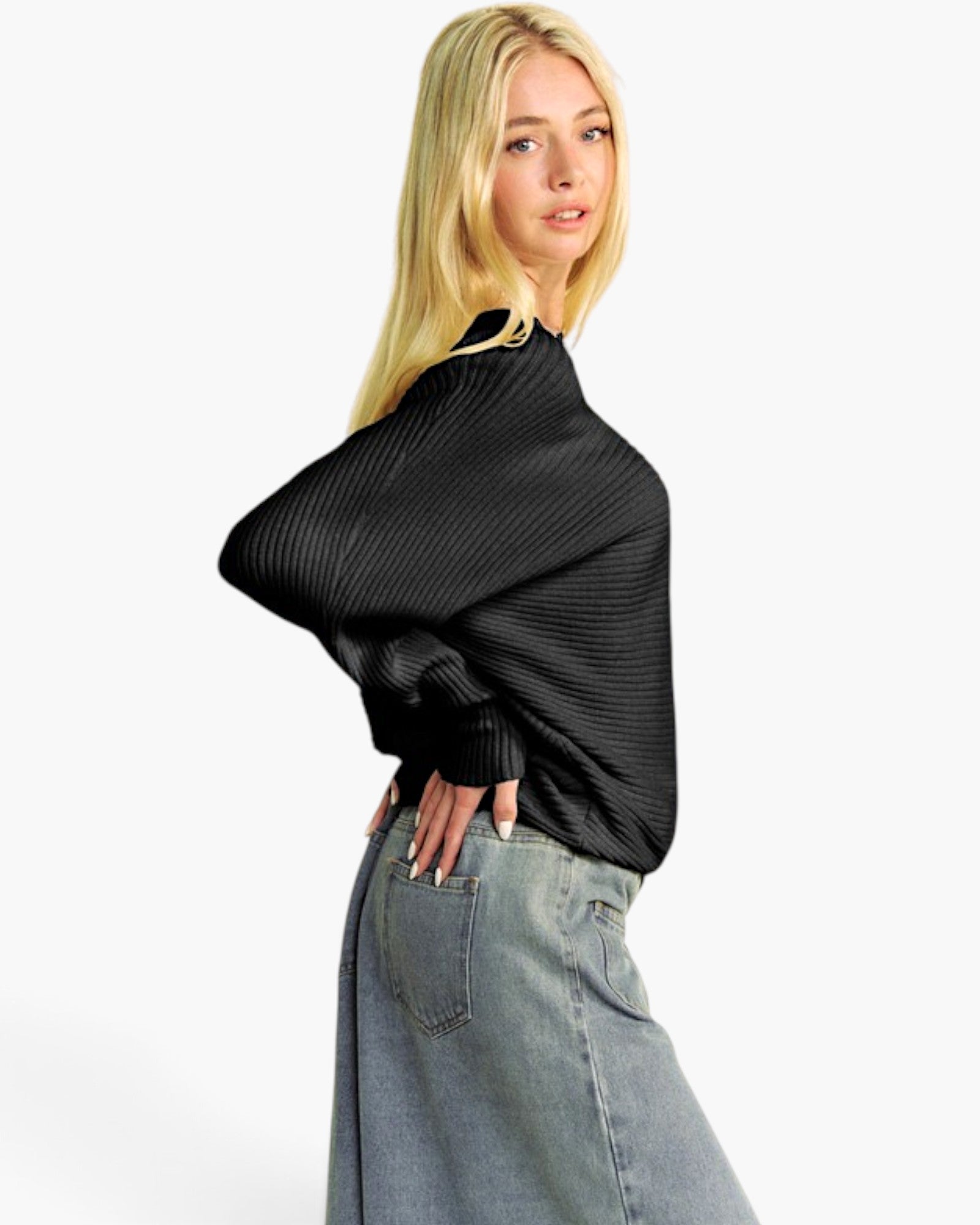 A blonde model wearing a black ribbed knit shrug or poncho-style top with wide draped sleeves, paired with light-wash denim skirt or shorts, photographed against a clean white studio background.