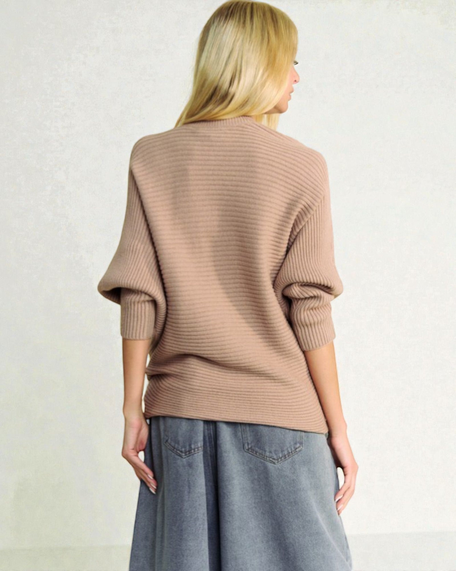 Person wearing a beige sweater and gray pants against a plain background