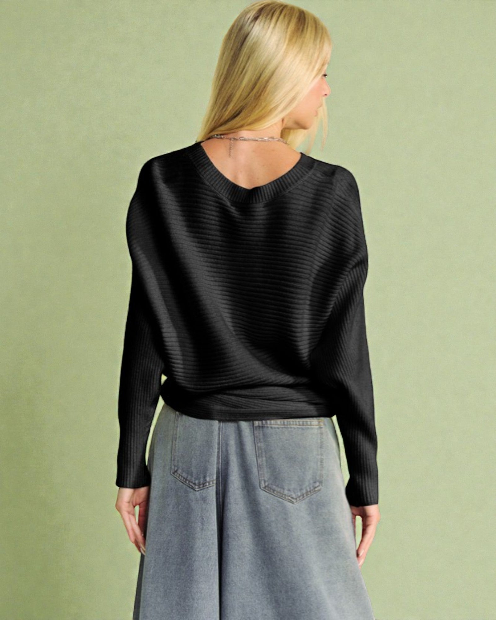 Woman wearing a black sweater and gray skirt against a green background