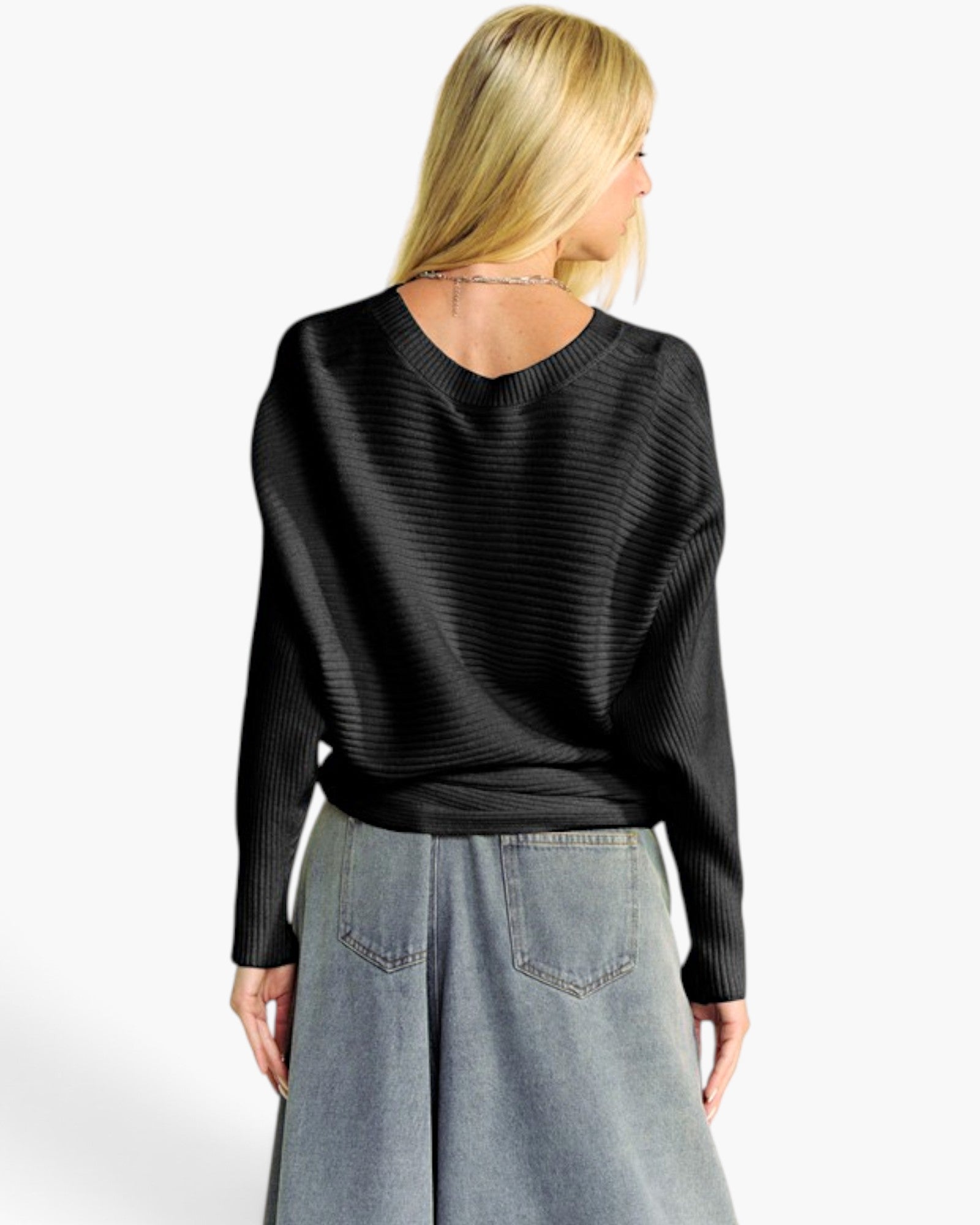 A woman shown from the back wearing a black ribbed long-sleeve sweater and a light blue denim skirt against a plain white studio background.