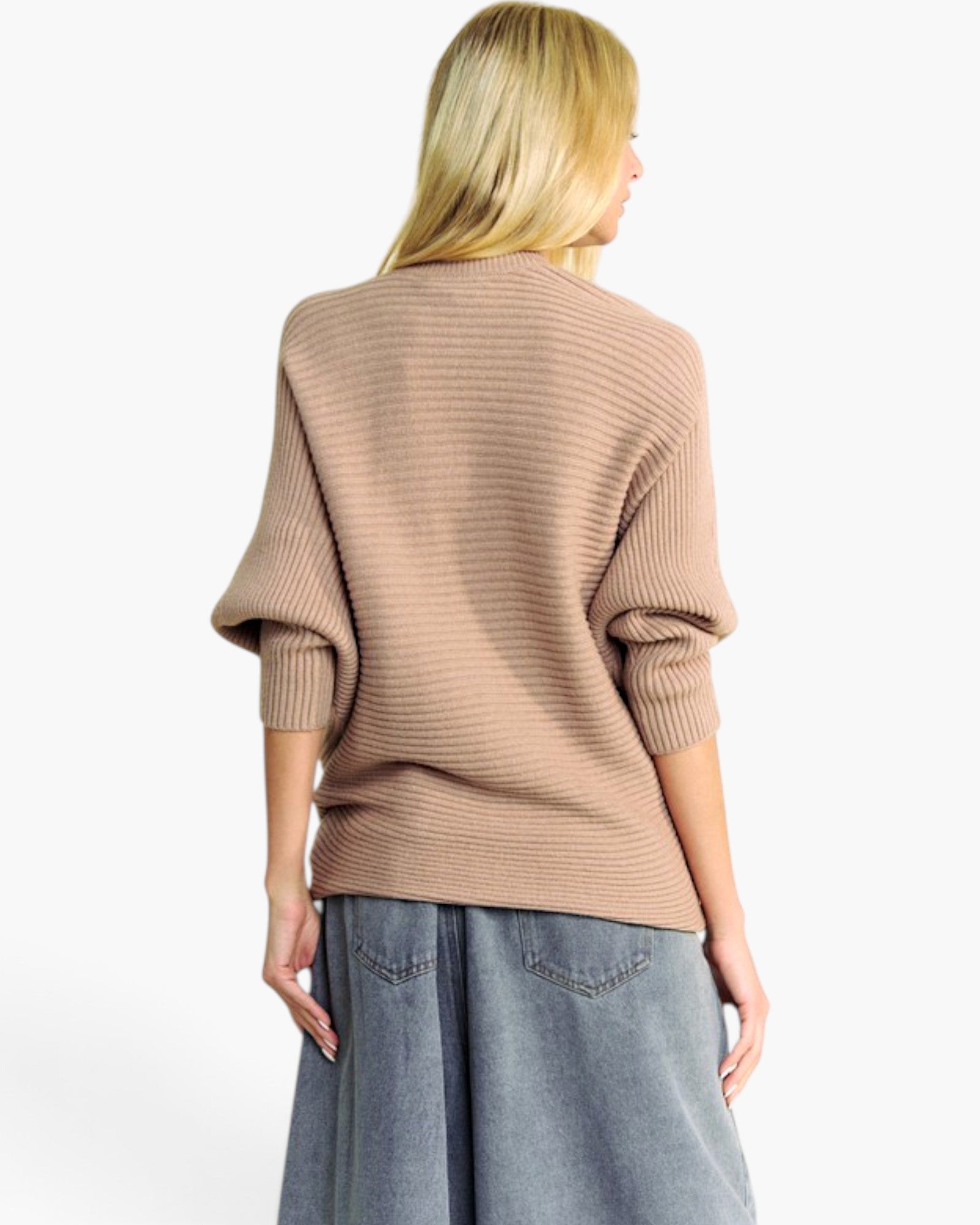 A woman shown from the back wearing a ribbed knit sweater in a warm taupe-beige color, paired with wide-leg denim jeans, against a plain white studio background.