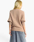 A woman shown from the back wearing a ribbed knit sweater in a warm taupe-beige color, paired with wide-leg denim jeans, against a plain white studio background.