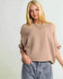 Woman wearing a beige sweater and blue jeans against a plain background