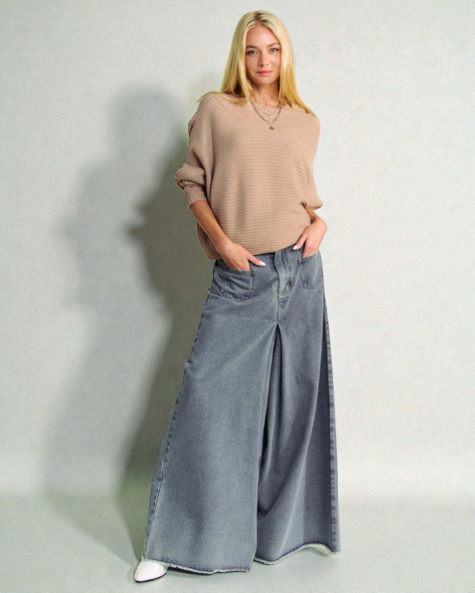 Woman wearing a beige sweater and blue wide-leg jeans against a plain background