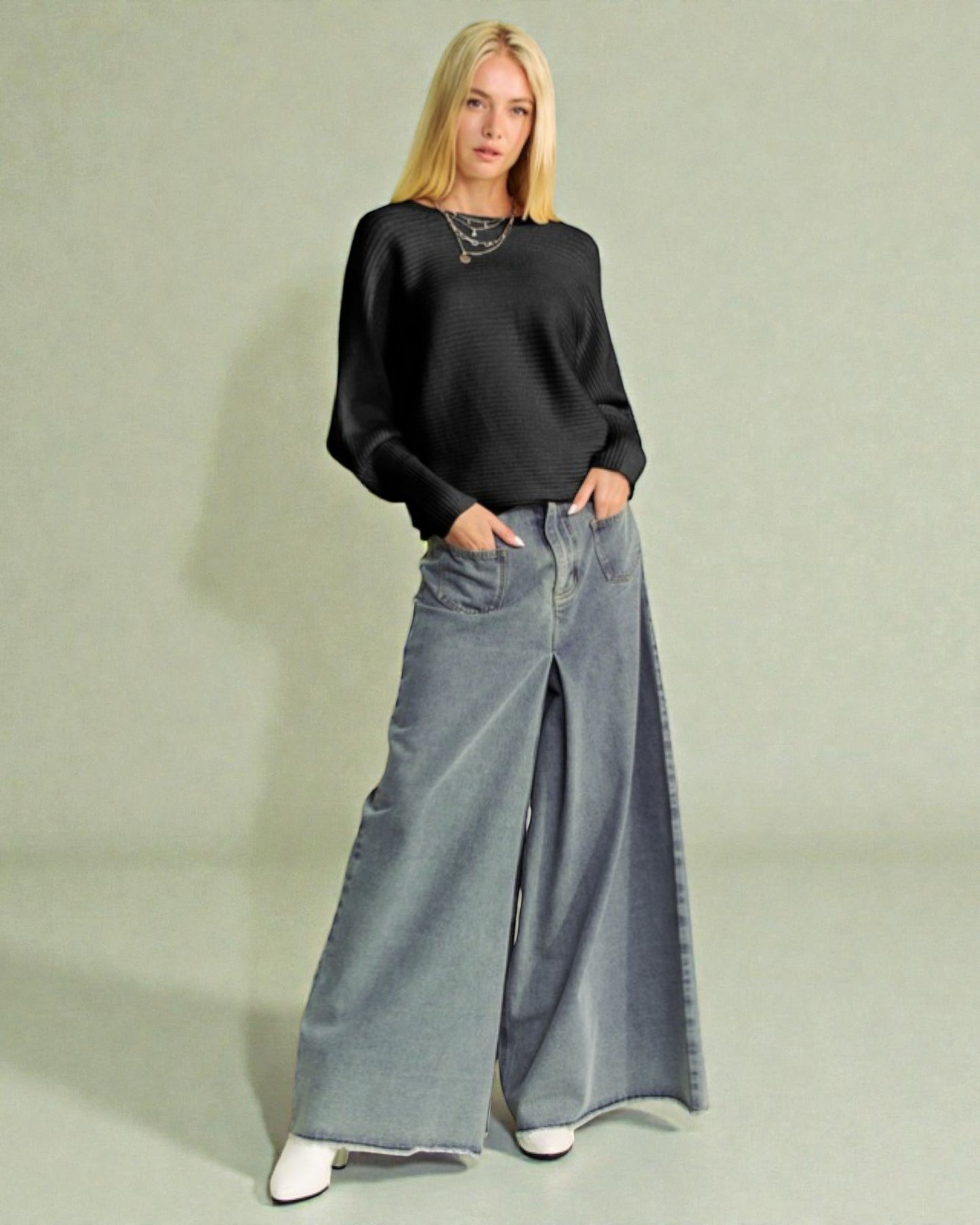 Woman wearing a black sweater and long denim skirt on a light green background