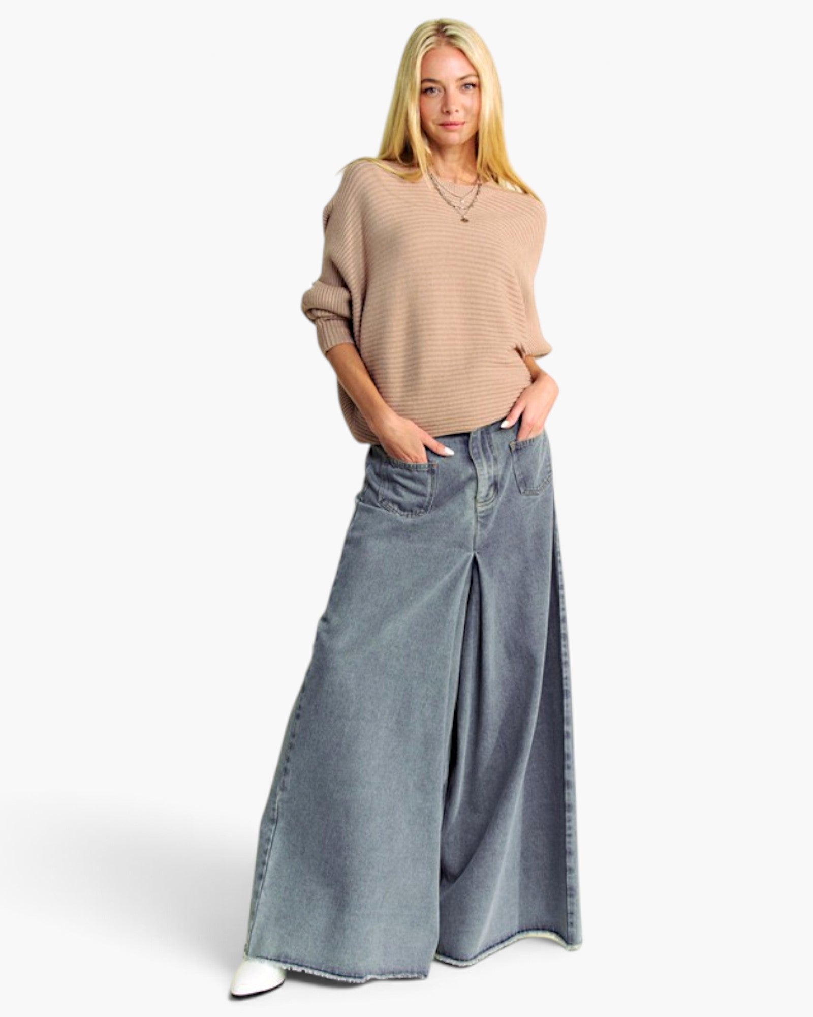 A blonde model wearing a beige ribbed knit sweater and wide-leg blue denim jeans, standing against a plain white studio background.