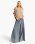 A blonde model wearing a beige ribbed knit sweater and wide-leg blue denim jeans, standing against a plain white studio background.