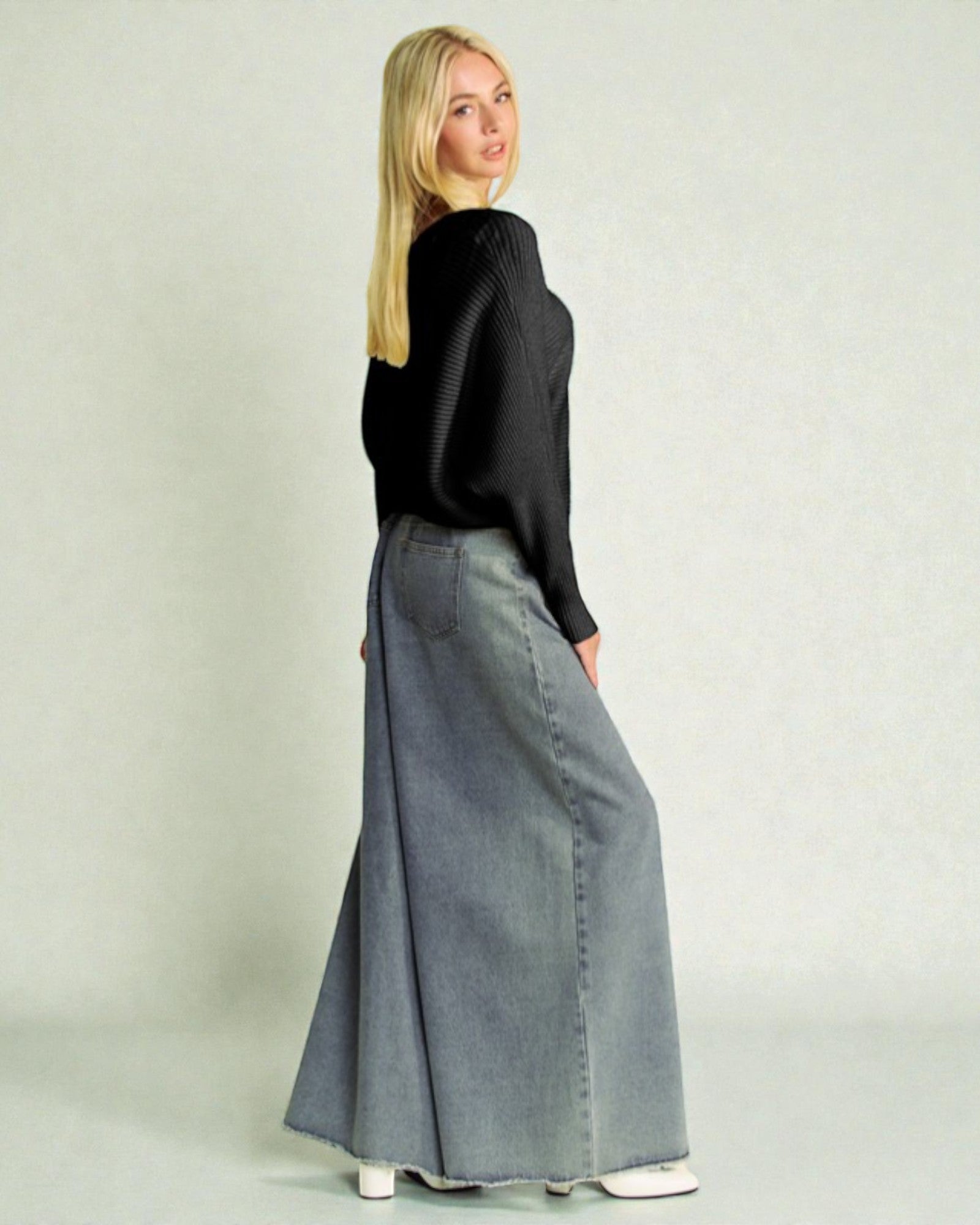 Woman wearing a black top and long denim skirt on a plain background