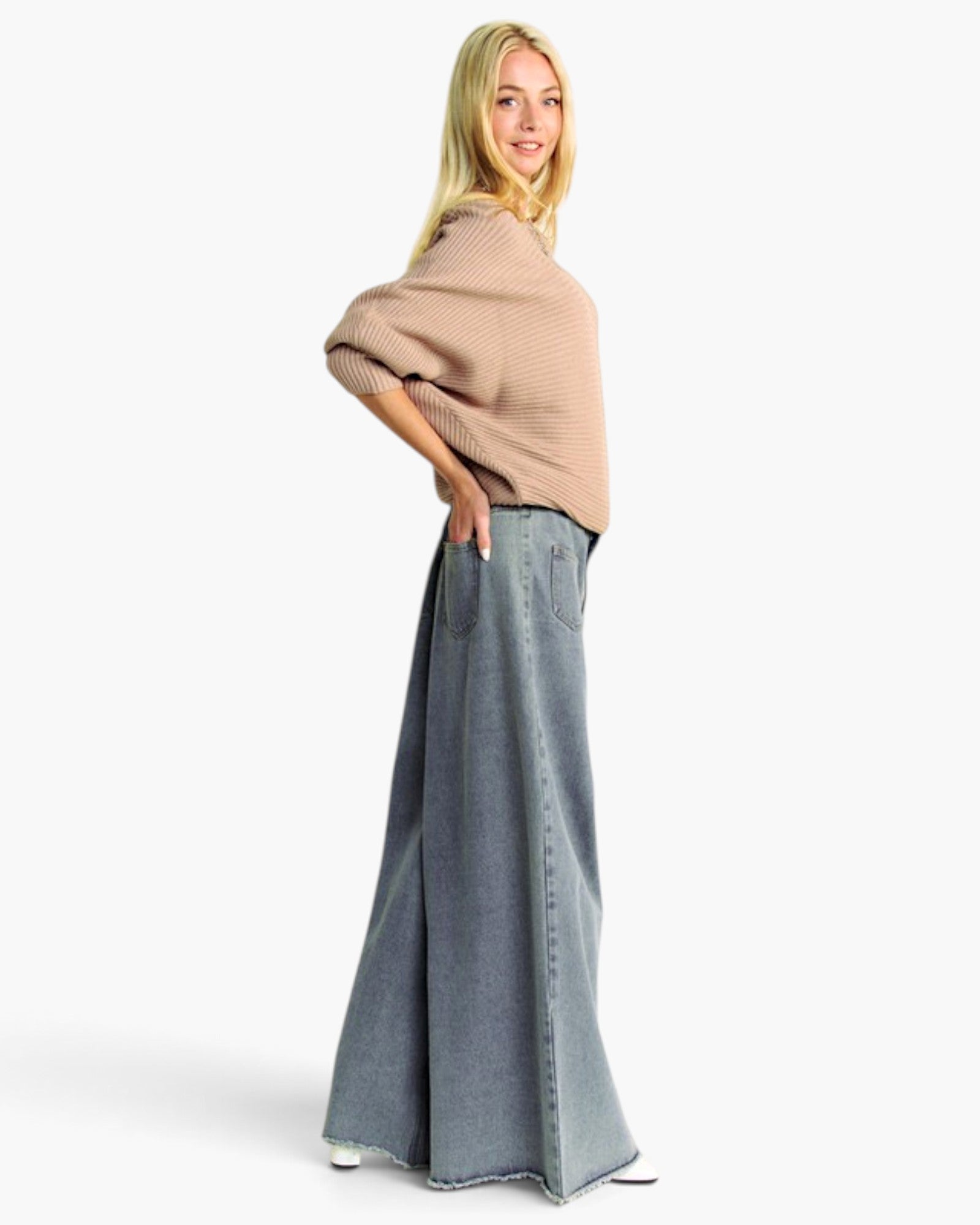 A woman modeling a beige knit poncho-style sweater and a wide-leg blue denim skirt against a plain white studio background.