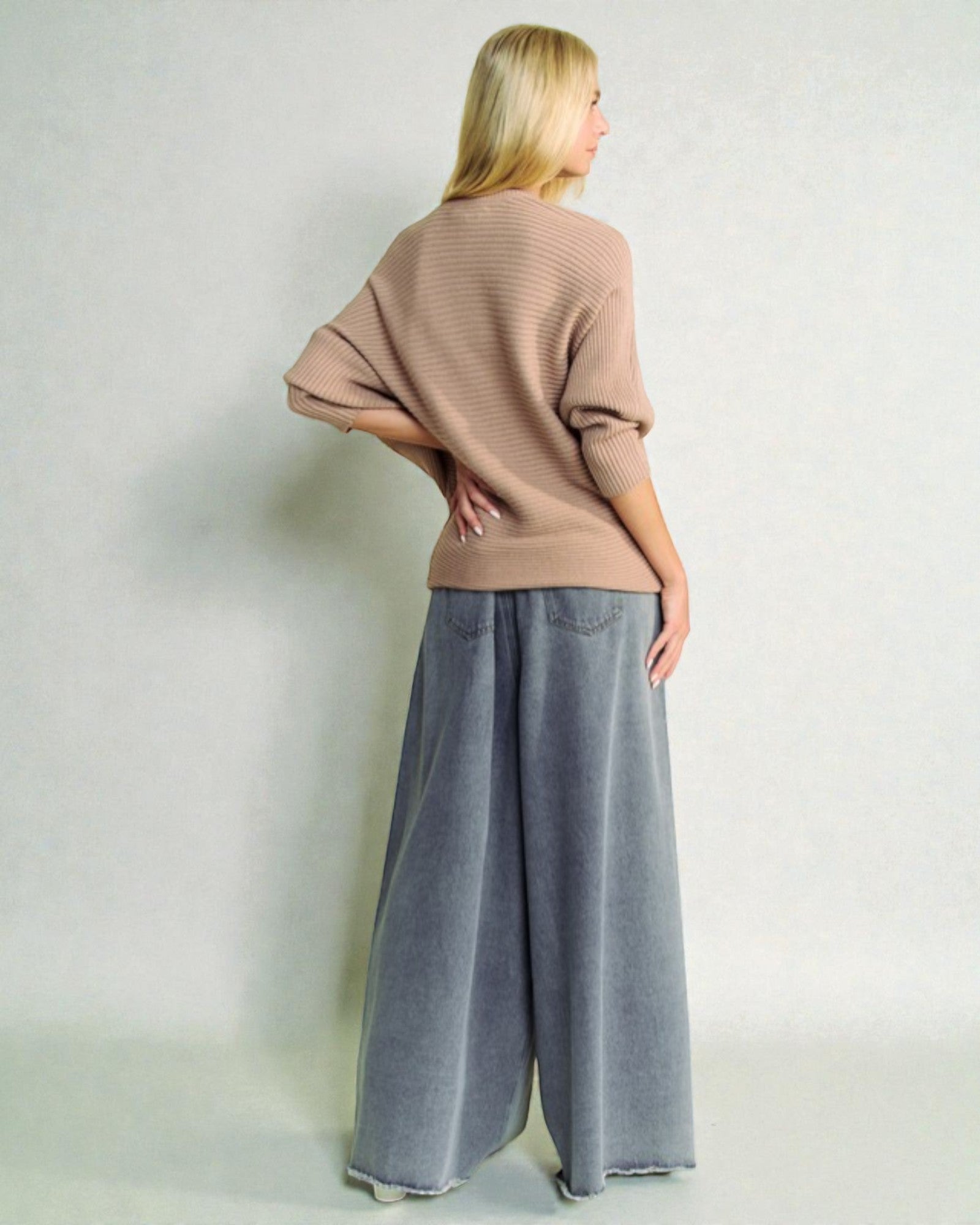 Woman wearing a beige sweater and gray wide-leg pants against a white background