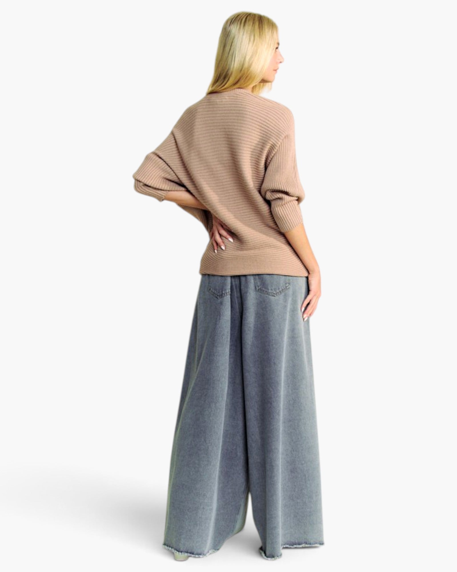 A woman shown from the back wearing a beige ribbed knit sweater and wide-leg gray jeans against a plain white studio background.