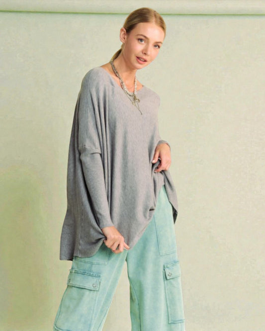 Woman wearing a gray oversized sweater and light blue cargo pants against a plain background