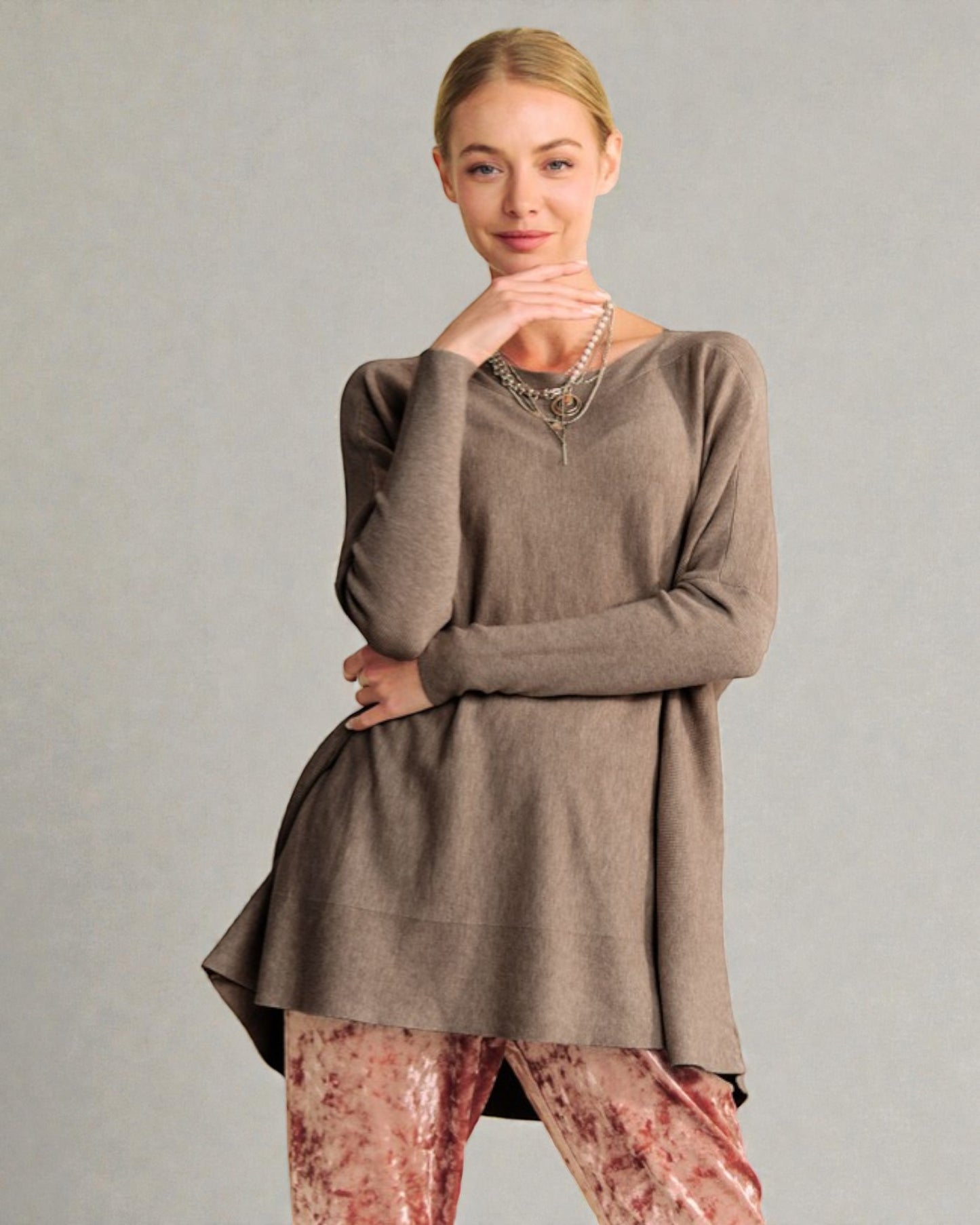 Woman wearing a brown long-sleeve top and patterned pants against a gray background