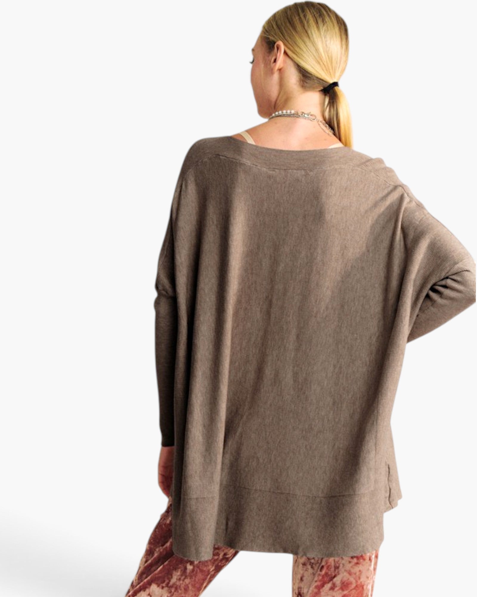 A woman shown from the back wearing a loose, long-sleeve taupe knit top and patterned leggings against a plain white studio background.