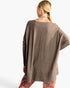 A woman shown from the back wearing a loose, long-sleeve taupe knit top and patterned leggings against a plain white studio background.