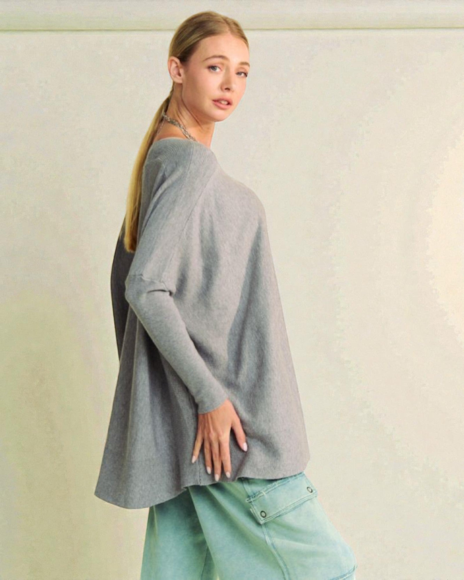 Woman wearing a gray sweater and light blue jeans against a plain background