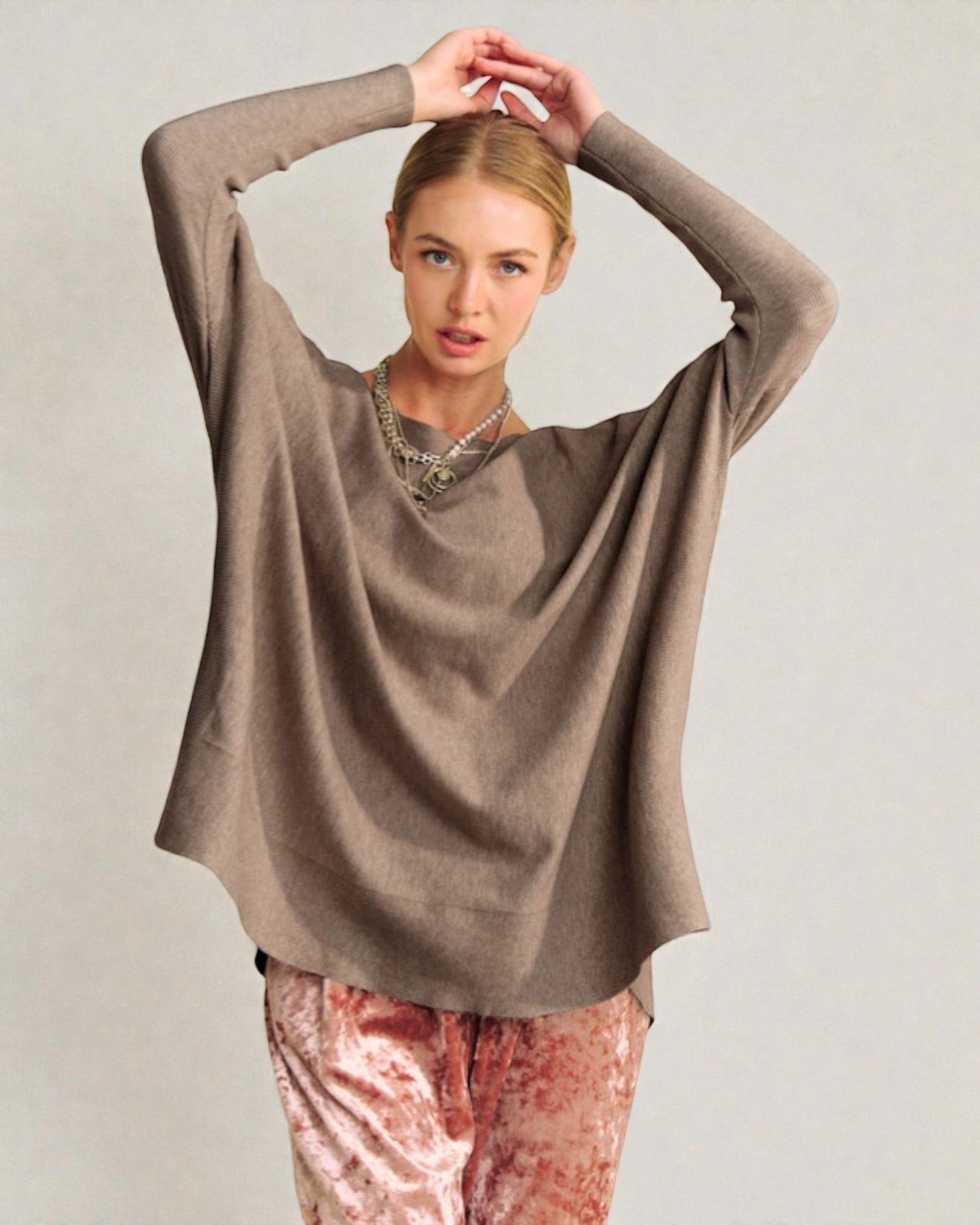 Woman wearing a brown sweater and pink pants against a plain background